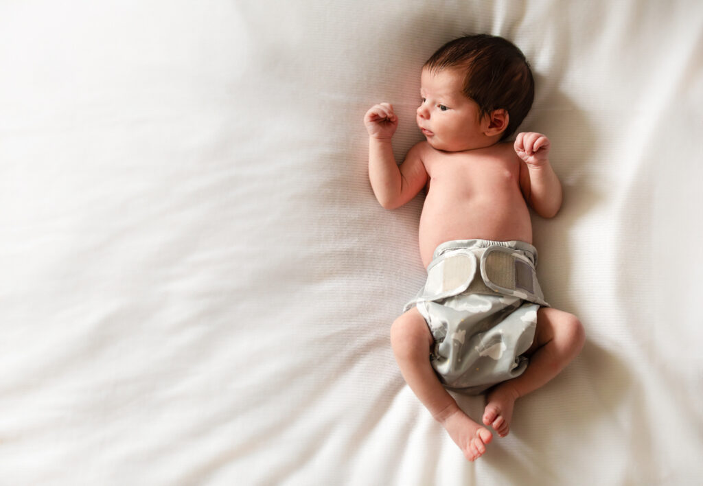 A newborn lays in a nappy on a clean white bed spread for a photo
