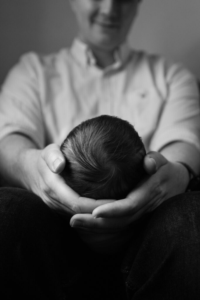 Newborn baby's head cradled in its fathers hands as he looks down at it with a smile