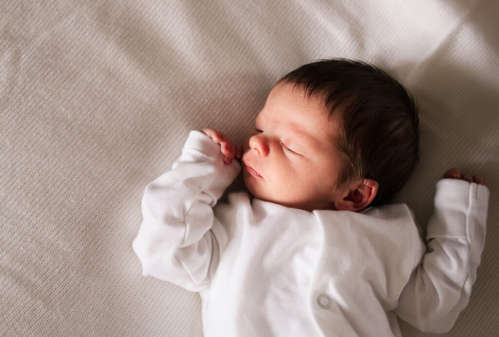 Relaxed newborn sleeps on the bed during his in-home photoshoot