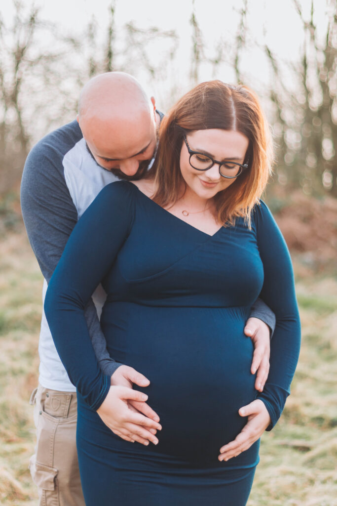 Parents to be gaze down lovingly at their baby bump with their hands resting gently on it