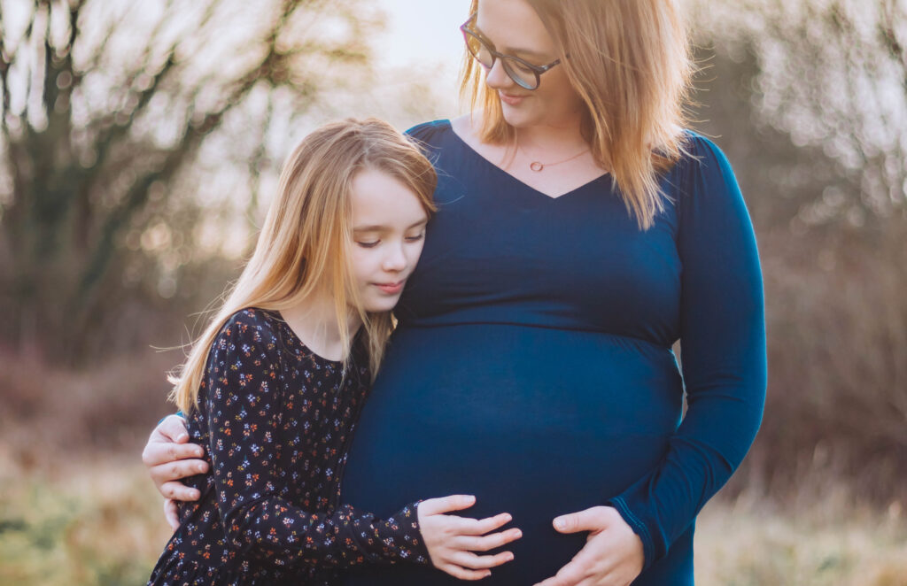 Mother and daughter embrace as they look down at the mums pregnant belly