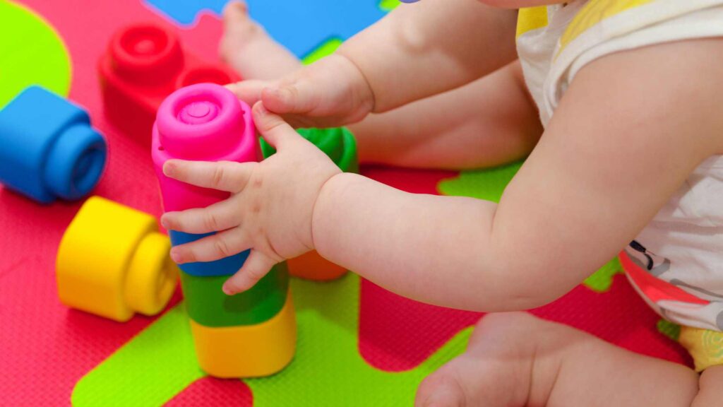 Baby plays with colourful tower of building blocks