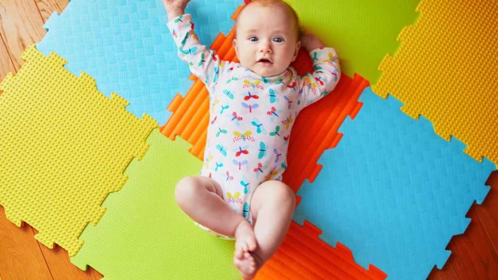 Baby in baby grow lays on a colourful play mat staring at the camera