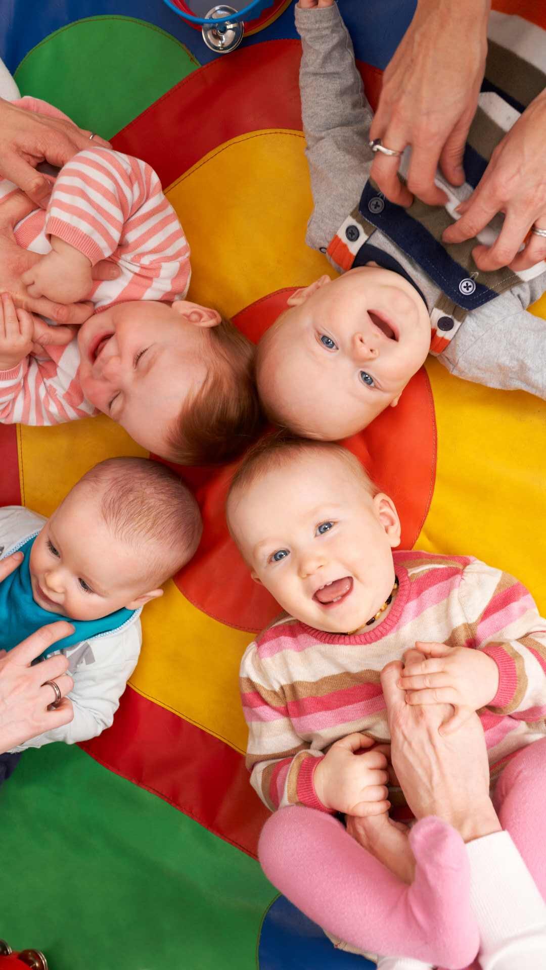 Babies lay on their backs being tickled by their adult during a Baby Class