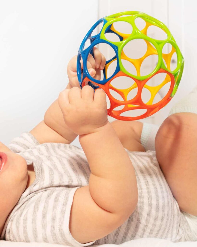 Baby lays on the ground playing with a plastic sensory ball