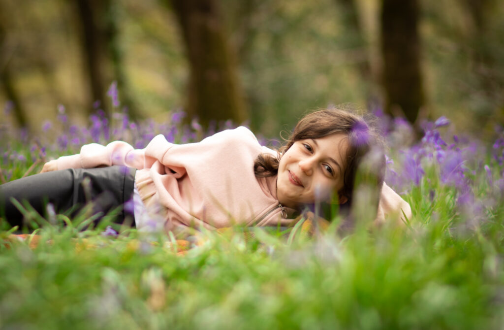 Young girl lays reclined among some bluebells smiling cheekily