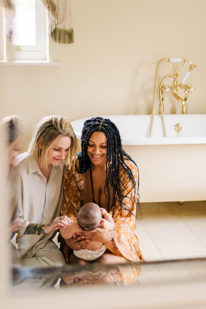 Couple sit on the bathroom floor as they smile down at their baby