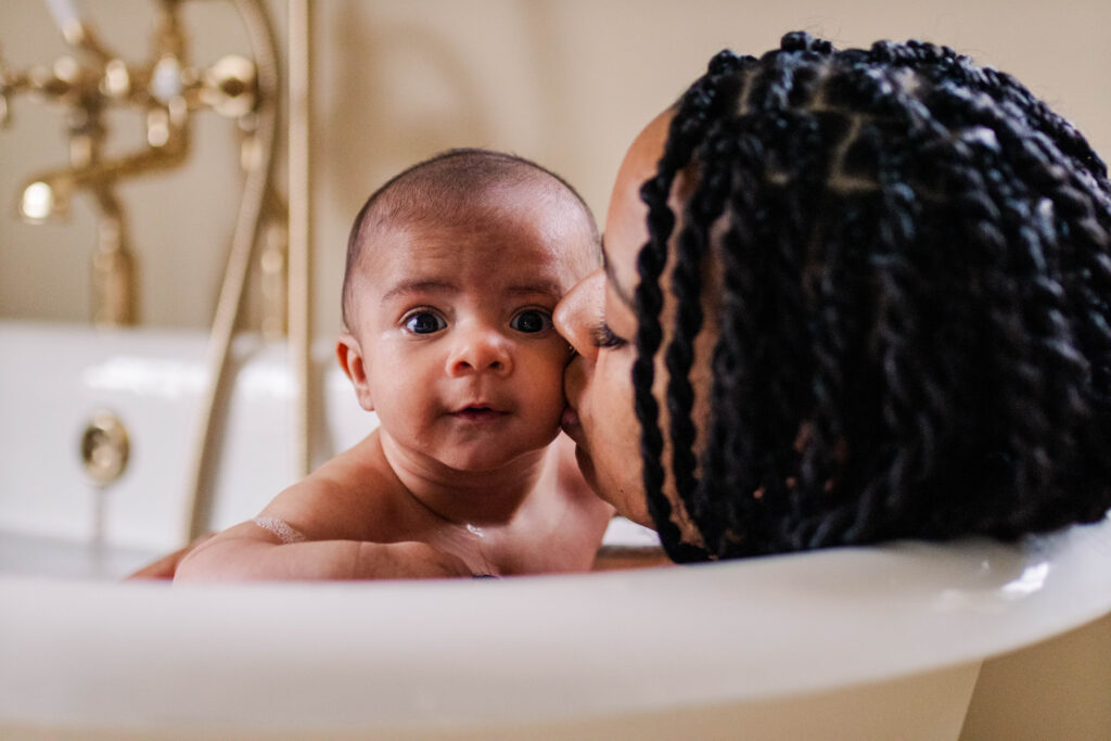 Mother kisses baby tenderly on the cheek as they lay in the bath