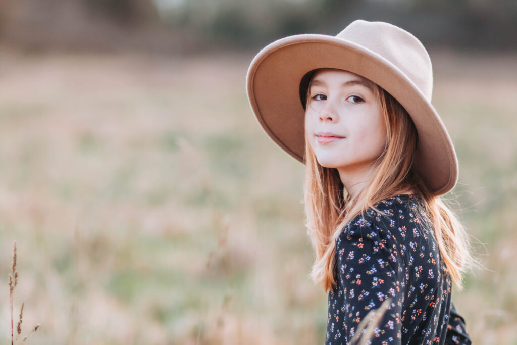 Young girl poses in a brown hat looking back over her shoulder at the camera.