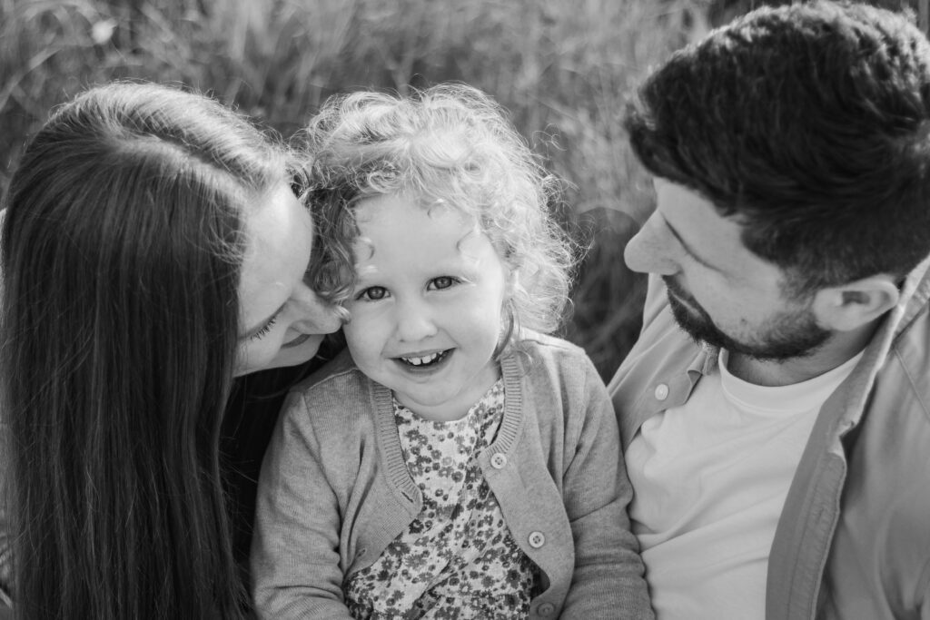 Little girl looks up at the camera as she sits between her parents at Ham Hill Country Park