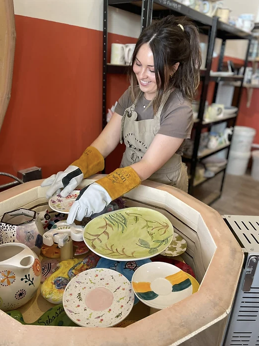 Lady wearing gloves removes fired items from a kiln.