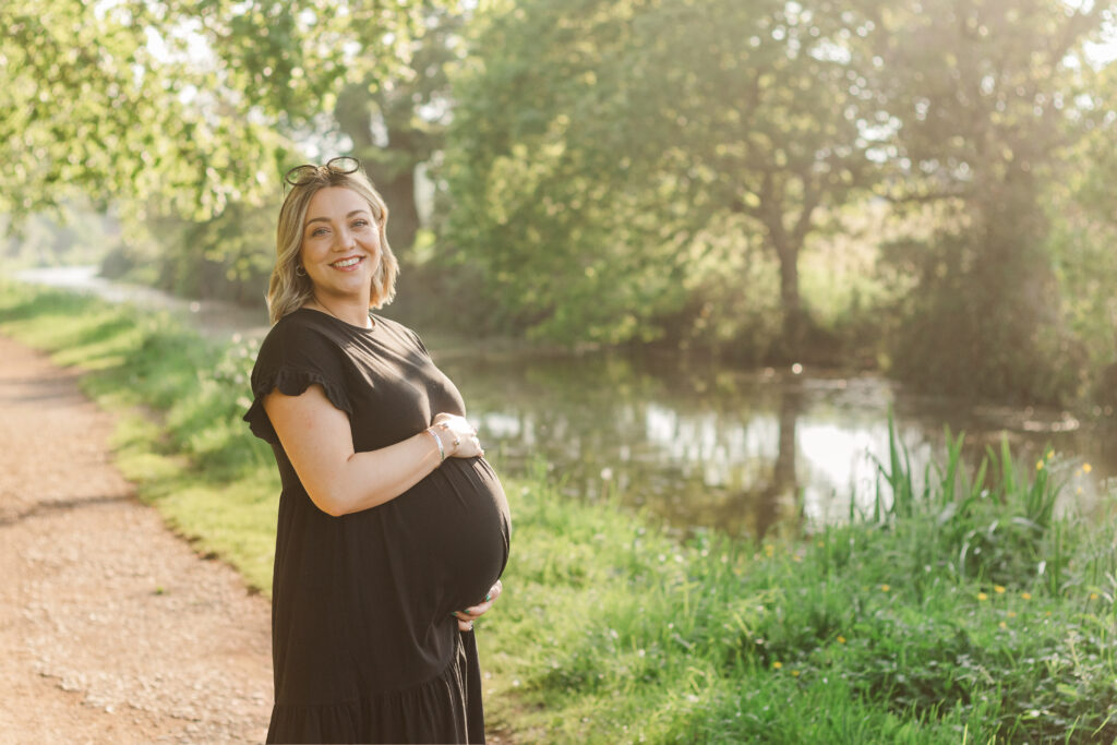 Mum to be stands holding her bump on the path of Taunton Canal