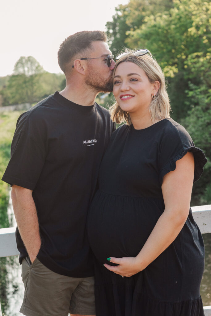 Husband kisses wife's head as she holds baby bump 