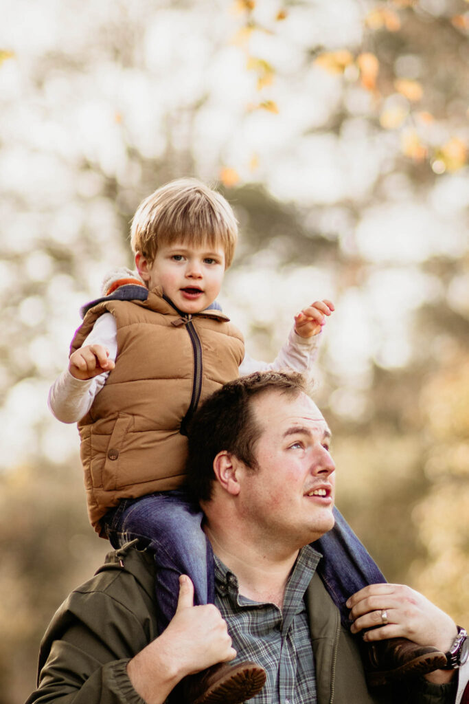 son sits atop father shoulder amongst autumn leaves