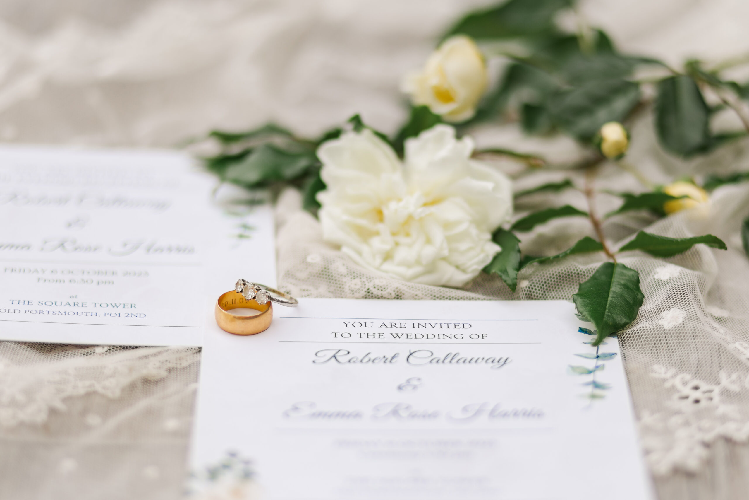 Wedding rings sitting atop wedding invitations, a lace veil