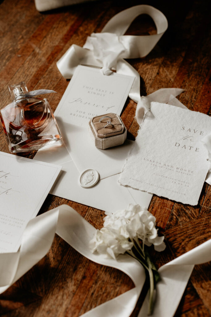 Flat lay of wedding details including rings, save the date cards and perfume