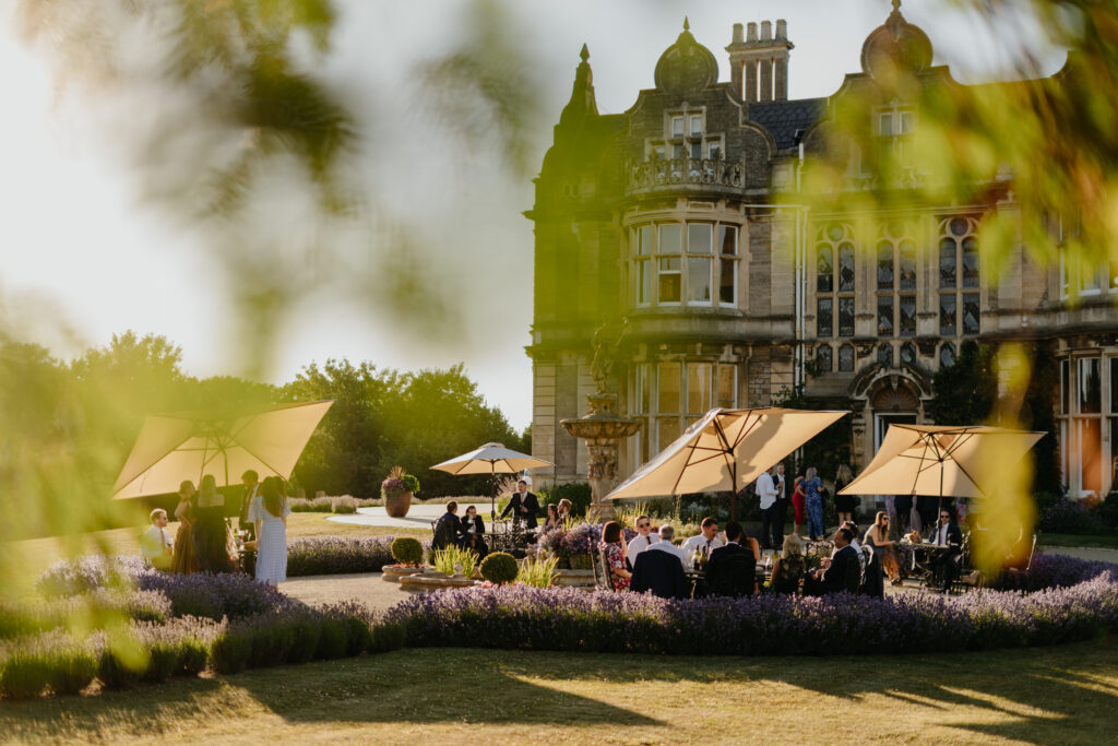 Wedding guests sit outside Clevedon Hall in the sunshine