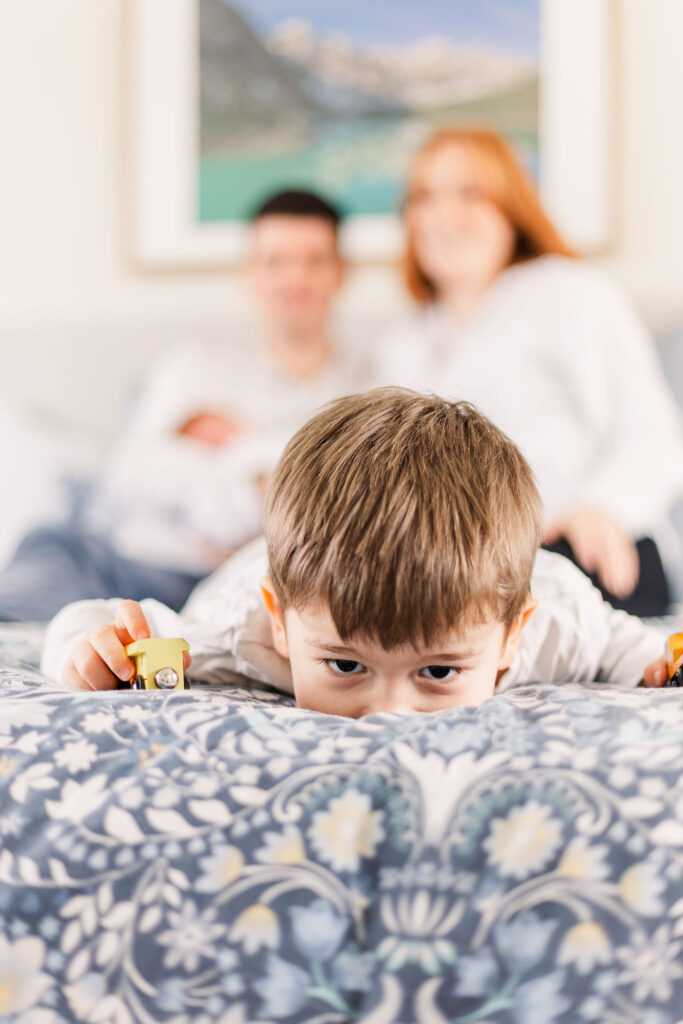 Toddler lays face down on the bed as parents look on