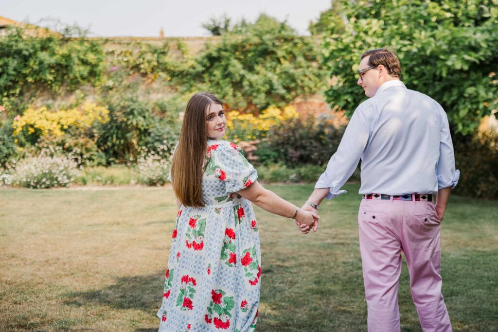 Couple hold hands and walk across the grass at Tintinhull Garden, Somerset