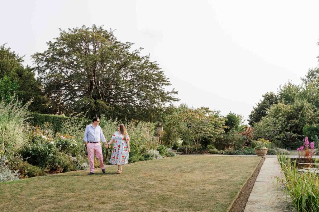 Walking hand in hand a engaged couple smile at each other during their photoshoot at Tintinhull Garden, Somerset
