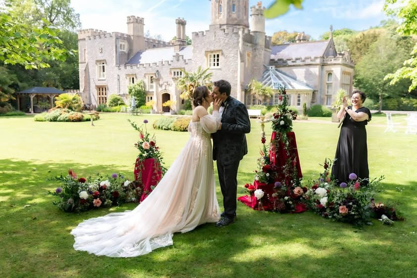 Wedding Celebrant looks on cheering as wedding couple share their first kiss as man and wife in castle grounds